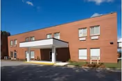 Brick senior living facility front entrance with a white canopy and parking.