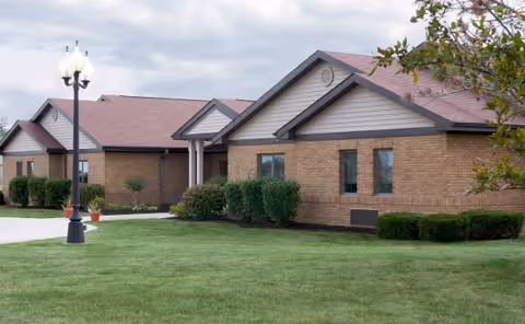 Single-story brick building with gabled roofs, a manicured lawn and a lamp post in front.