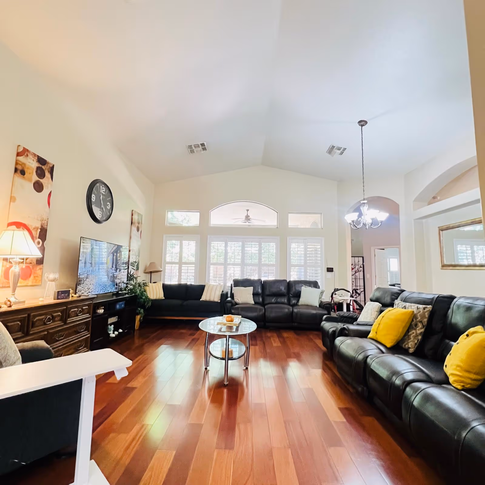 Spacious living room with black leather sofas, glass coffee table, wooden floor, and large windows.