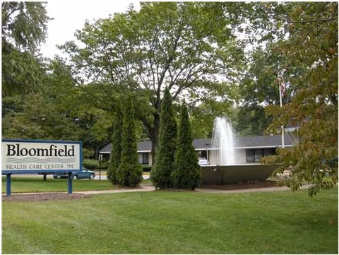 Exterior view of Bloomfield Health Care Center with fountain, sign, and green lawn.