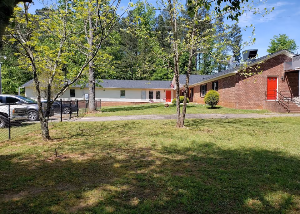 Exterior view of a single-story brick facility with red doors, green lawn, and trees.