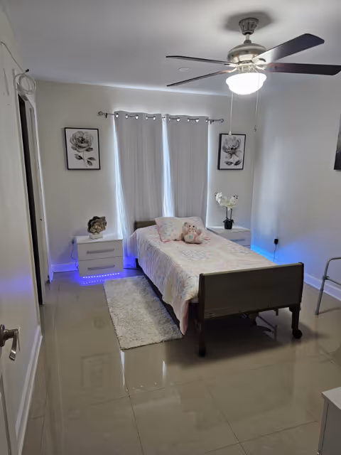 A neatly made bedroom with a single bed, two nightstands, ceiling fan, and blue accent lighting.