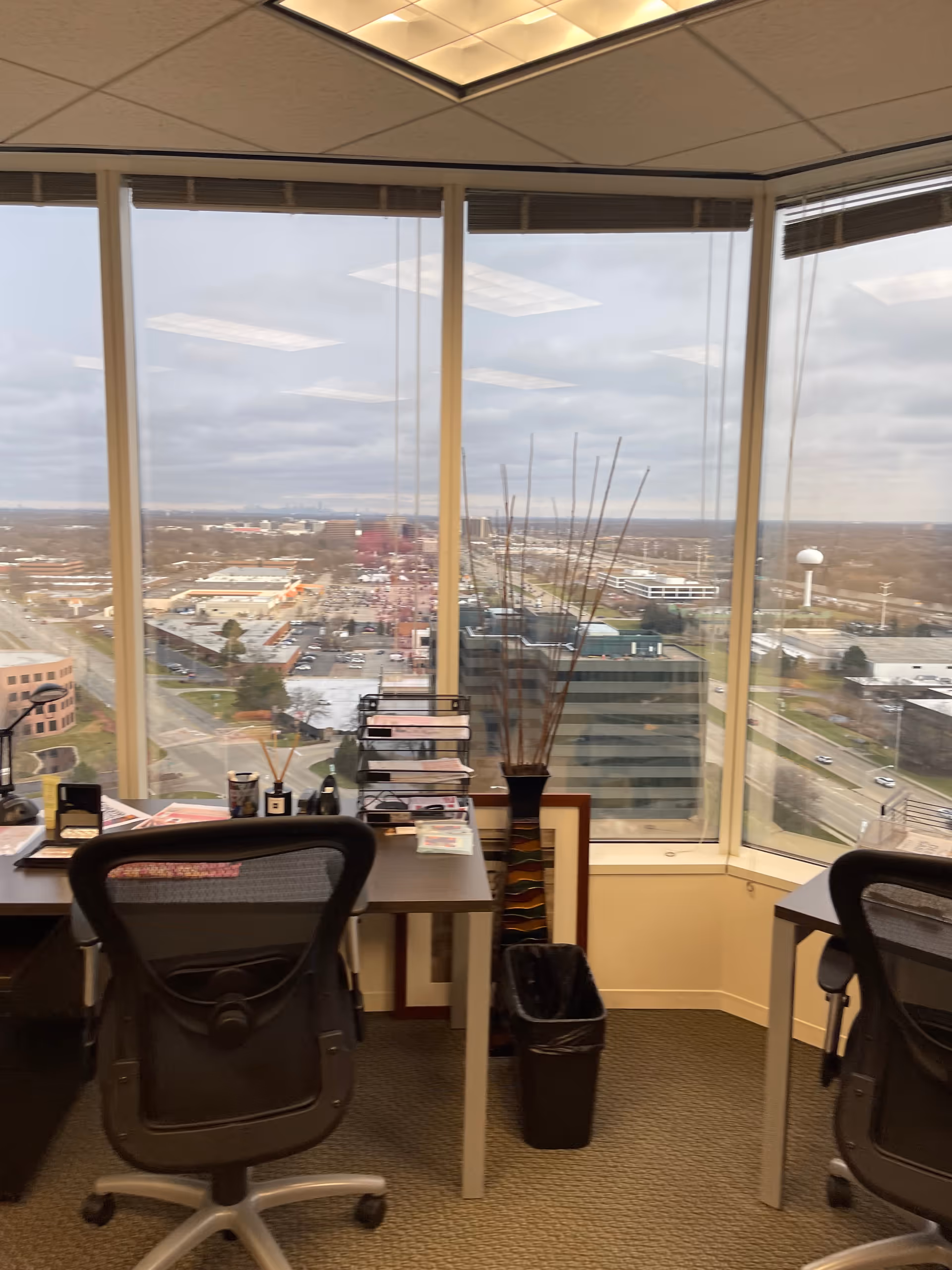 Office workspace with two desks, chairs, and a large window overlooking the city.