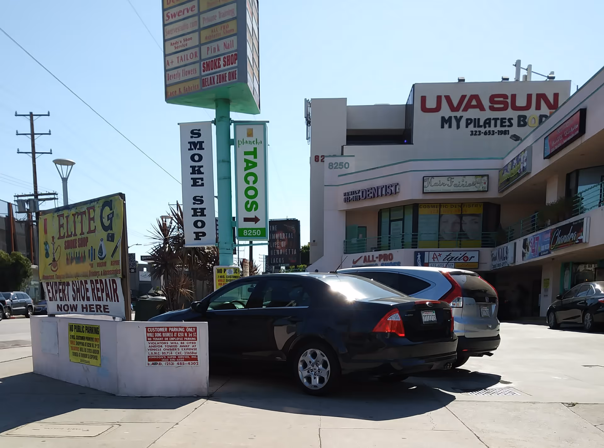Busy storefronts on a sunny street with parked cars in front of buildings.
