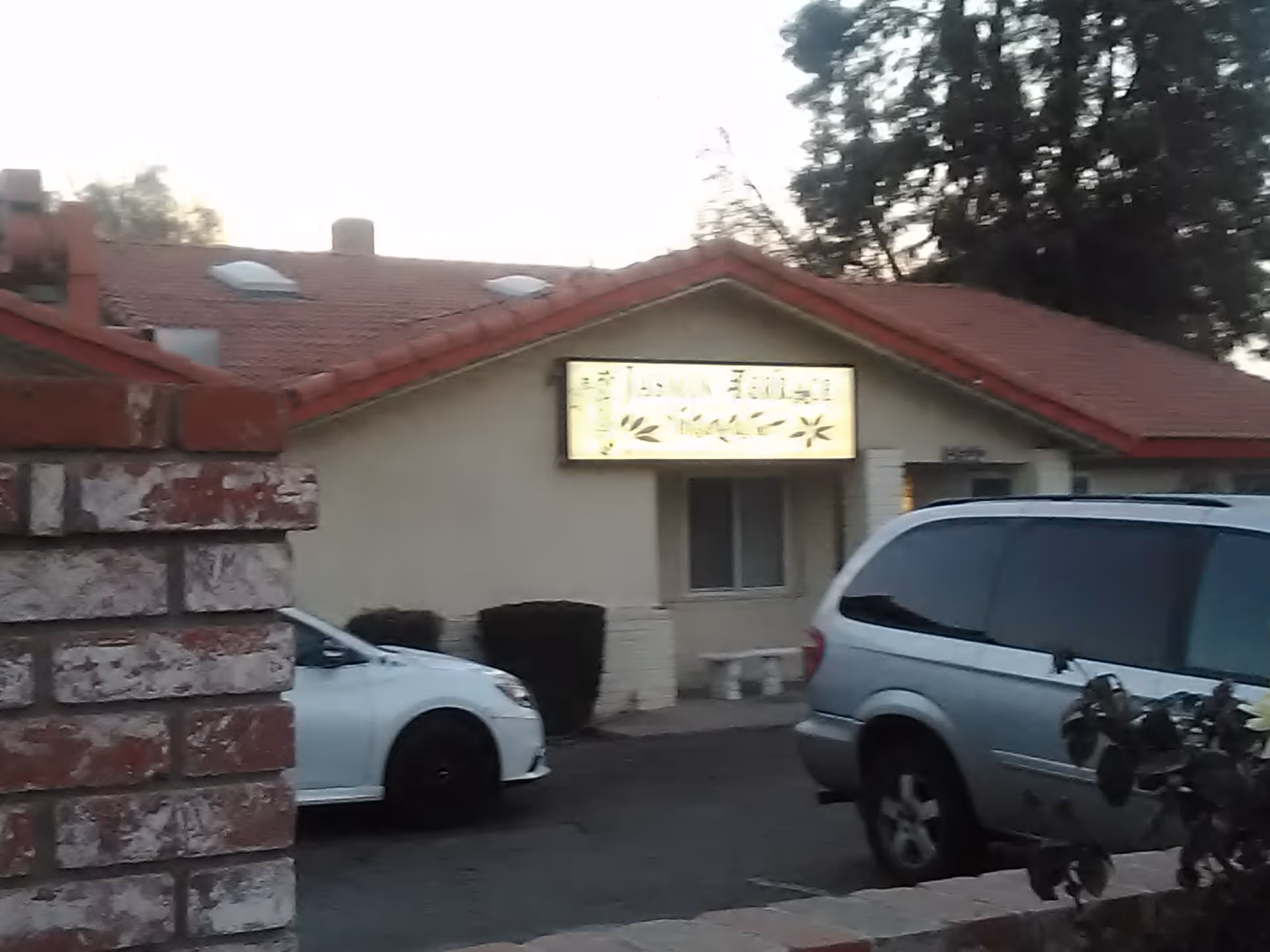 Front exterior of a single-story senior living facility with an illuminated sign and cars.