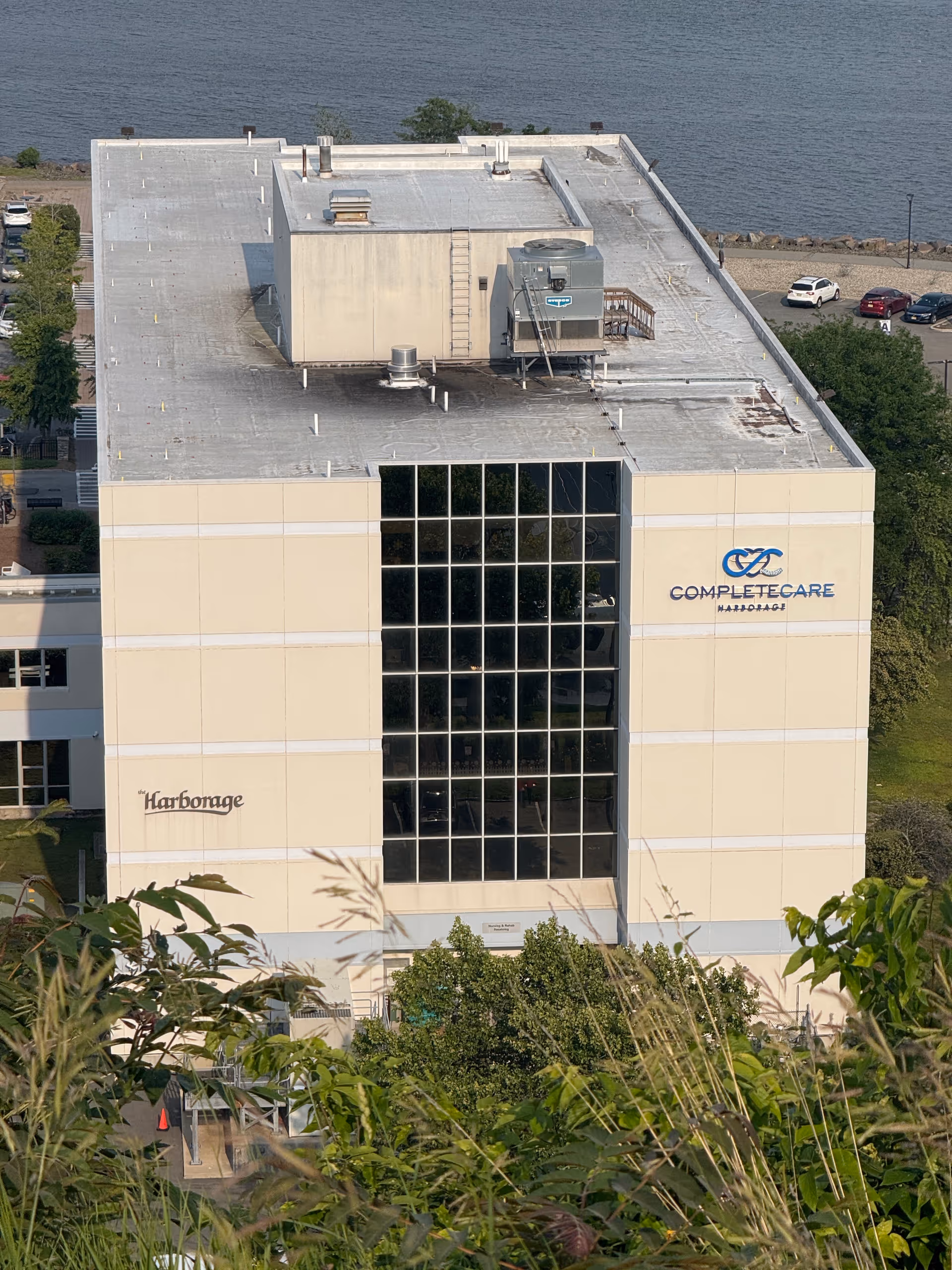 Aerial view of a beige multi-story senior living building by the water with glass facade.