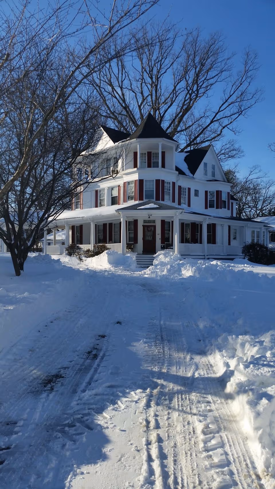 Snow-covered two-story house with a wide front porch and bare trees.