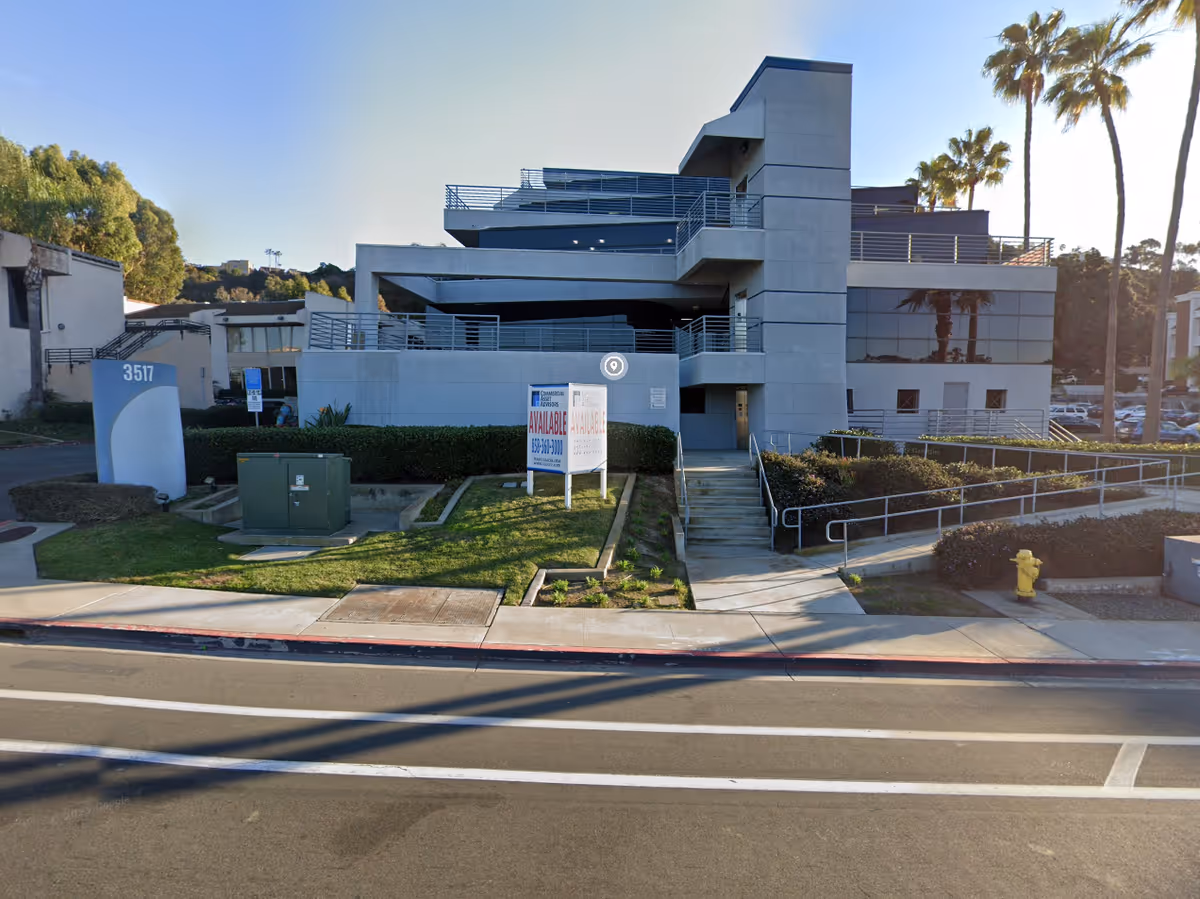Modern multi-level senior living building on a street with palm trees and signage