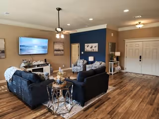 A spacious senior living facility living room with seating, TV, and artwork.