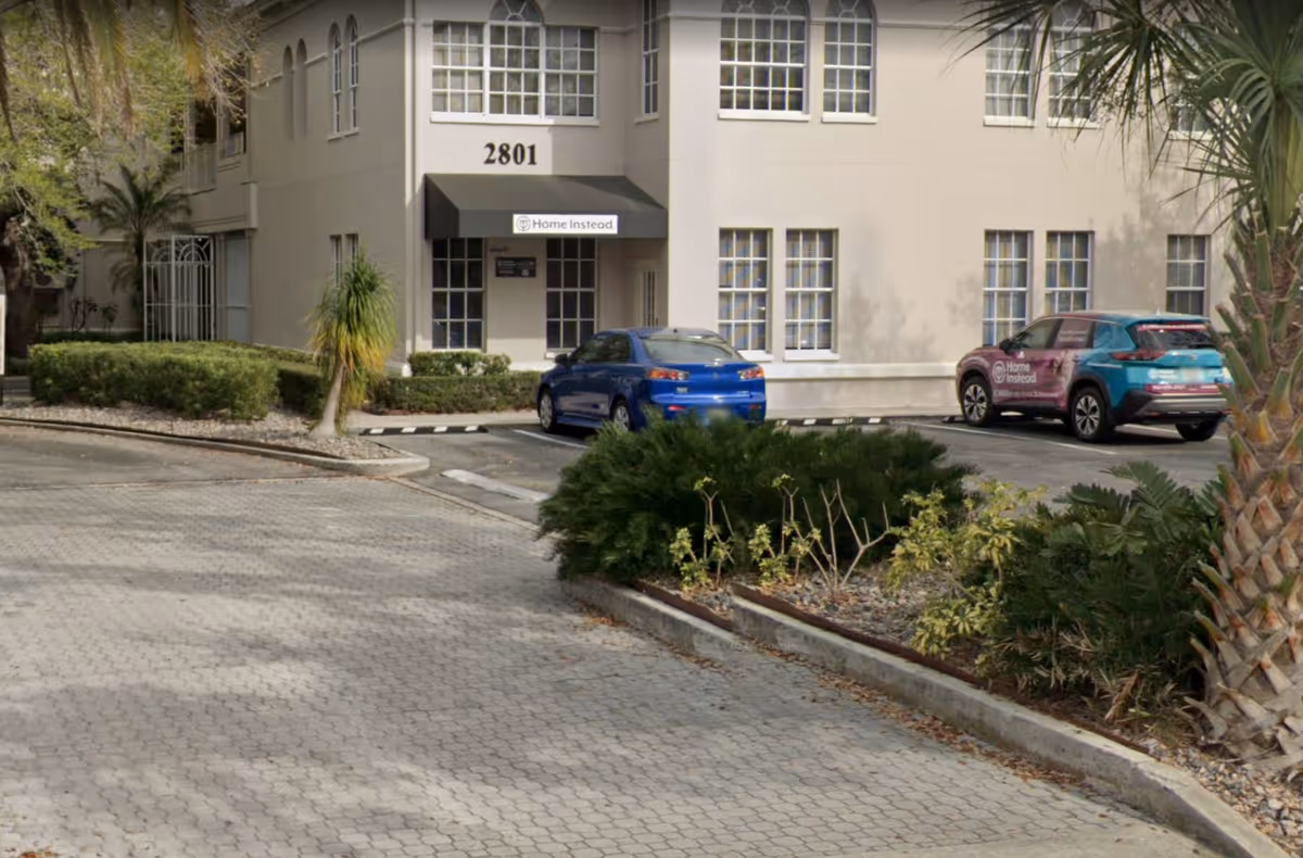 Exterior view of a building with Home Instead sign, entrance, and parked cars.