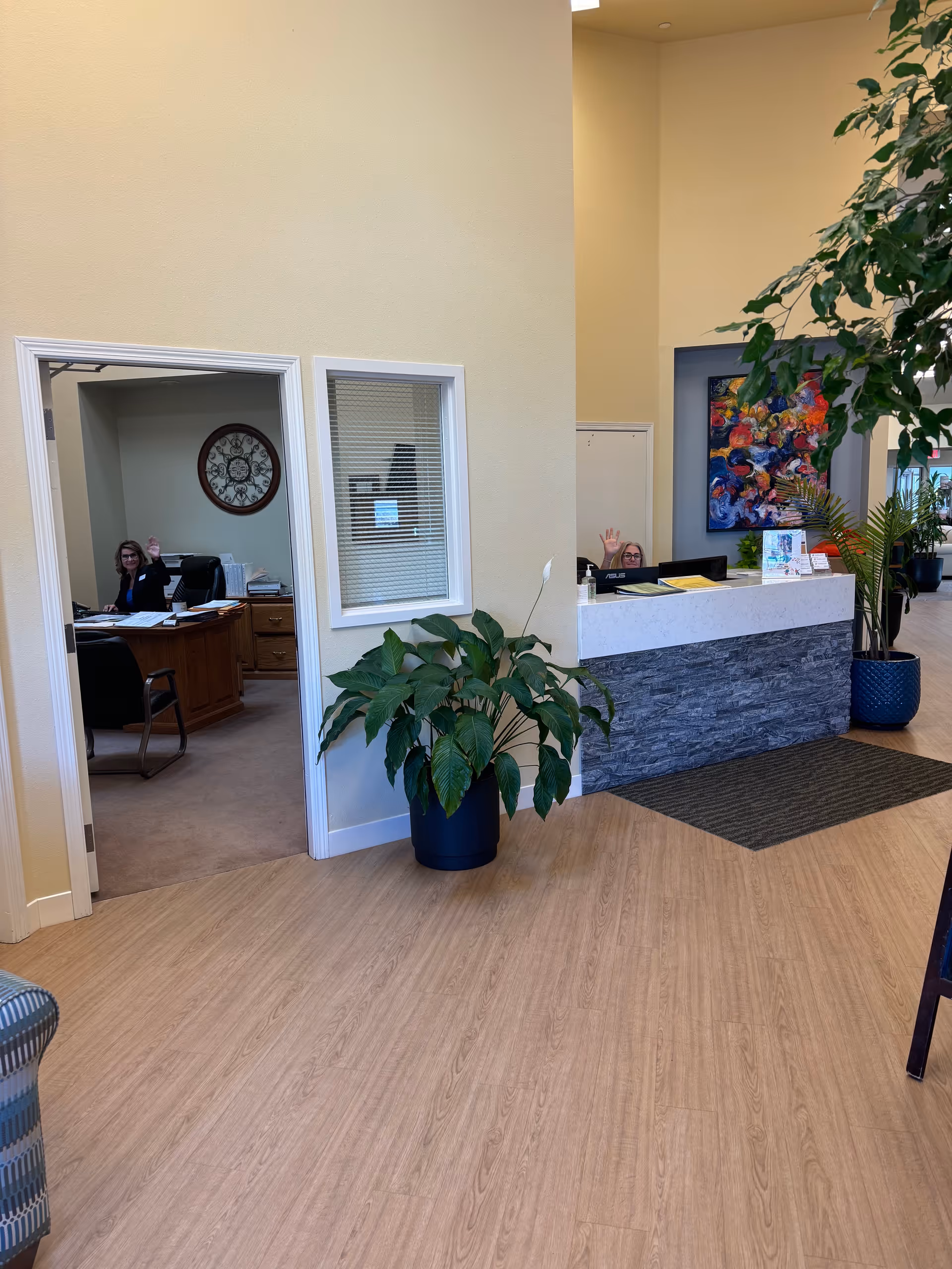 Reception area of Colonial Court lobby with a waving receptionist, plants, and artwork.