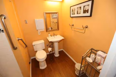 Small bathroom with toilet, pedestal sink, mirror, towel rack, and cart in orange-walled room.