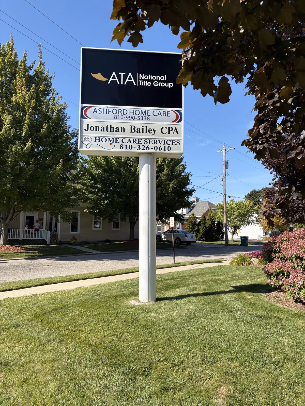 Tall sign on a pole advertising Ashford Home Care in a grassy area by a street.
