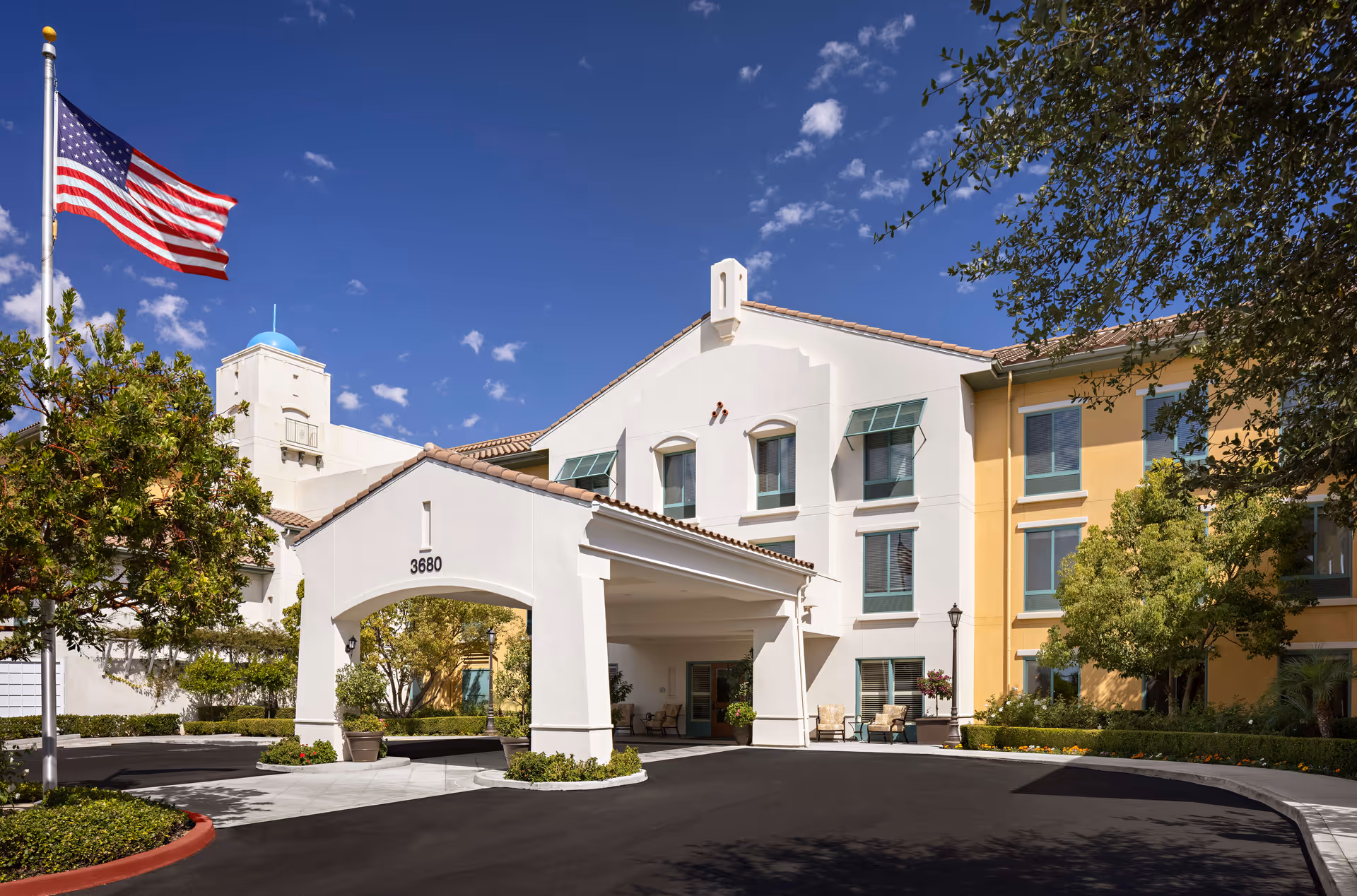Exterior view of Belmont Village Senior Living Thousand Oaks, showing entrance canopy and flag.