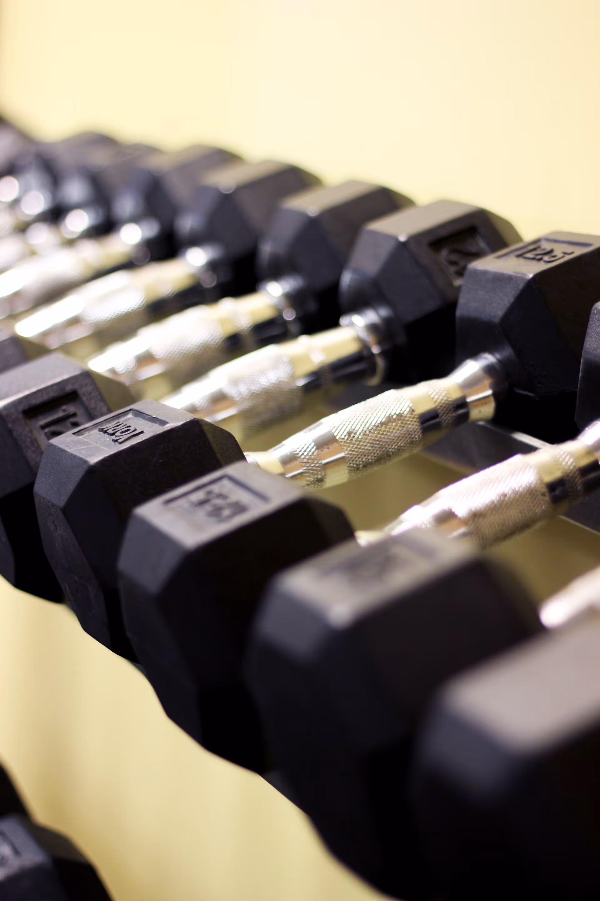 Row of black hex dumbbells on a chrome rack in a gym.