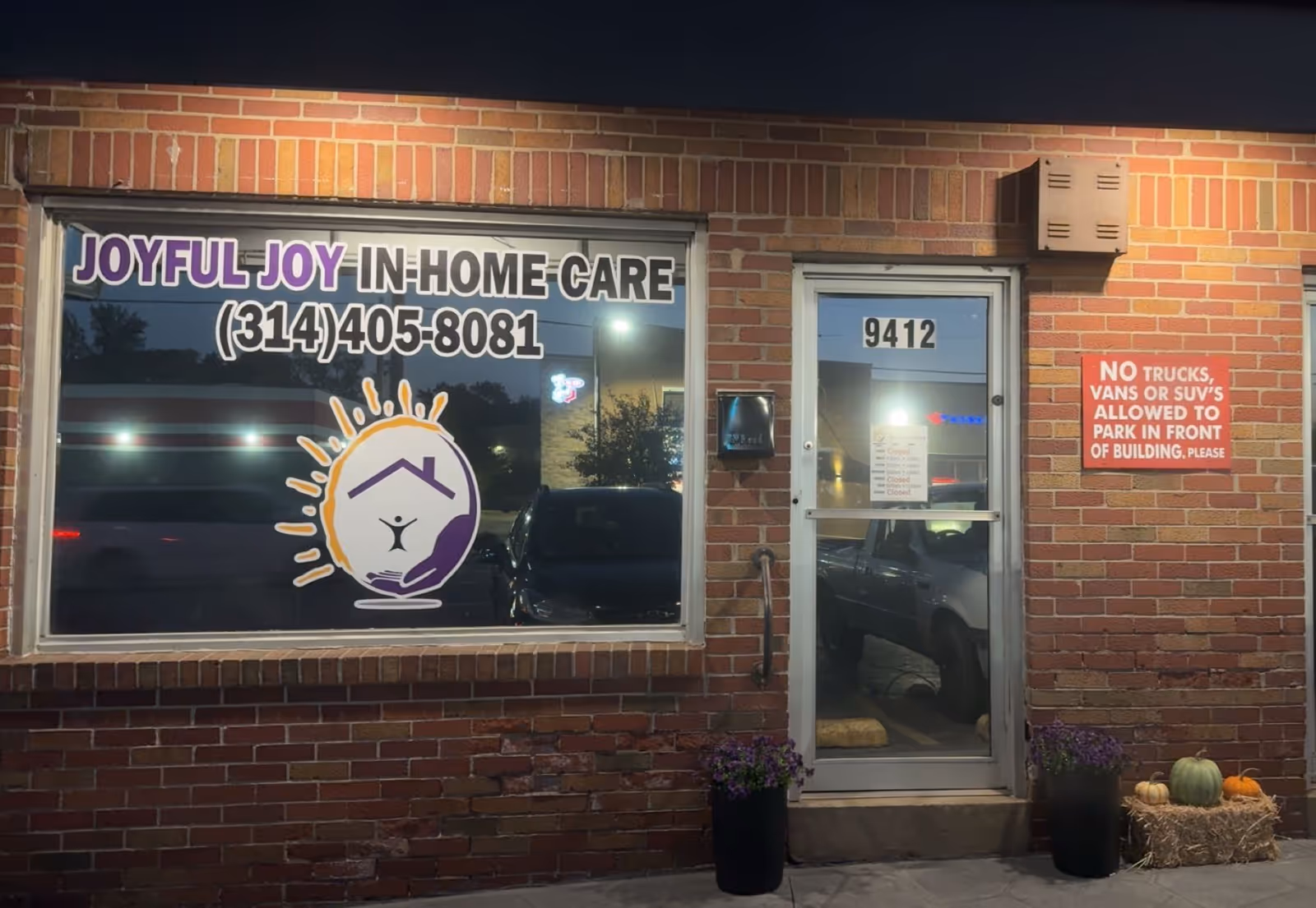 Brick storefront with JOYFUL JOY IN-HOME CARE sign, front door, and pumpkins outside.
