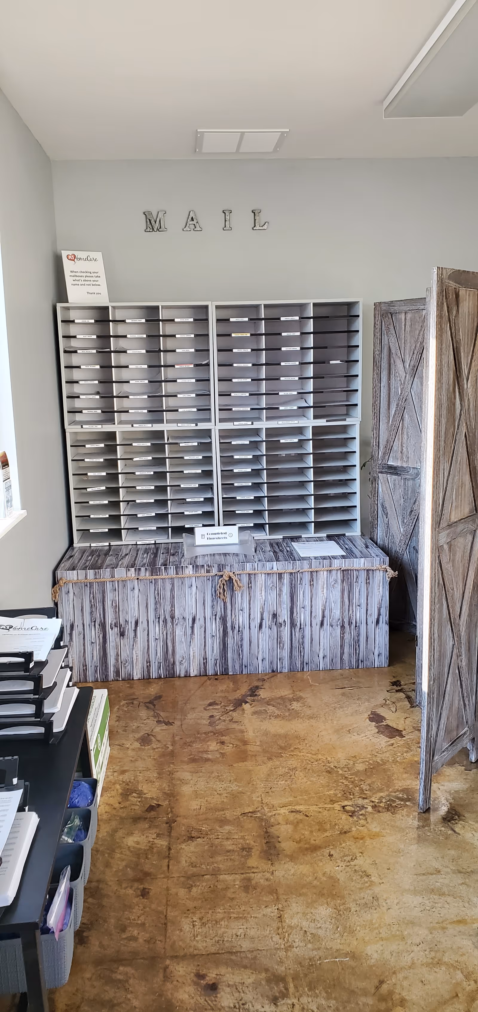 Indoor mail station with many letter slots and rustic storage cabinet.
