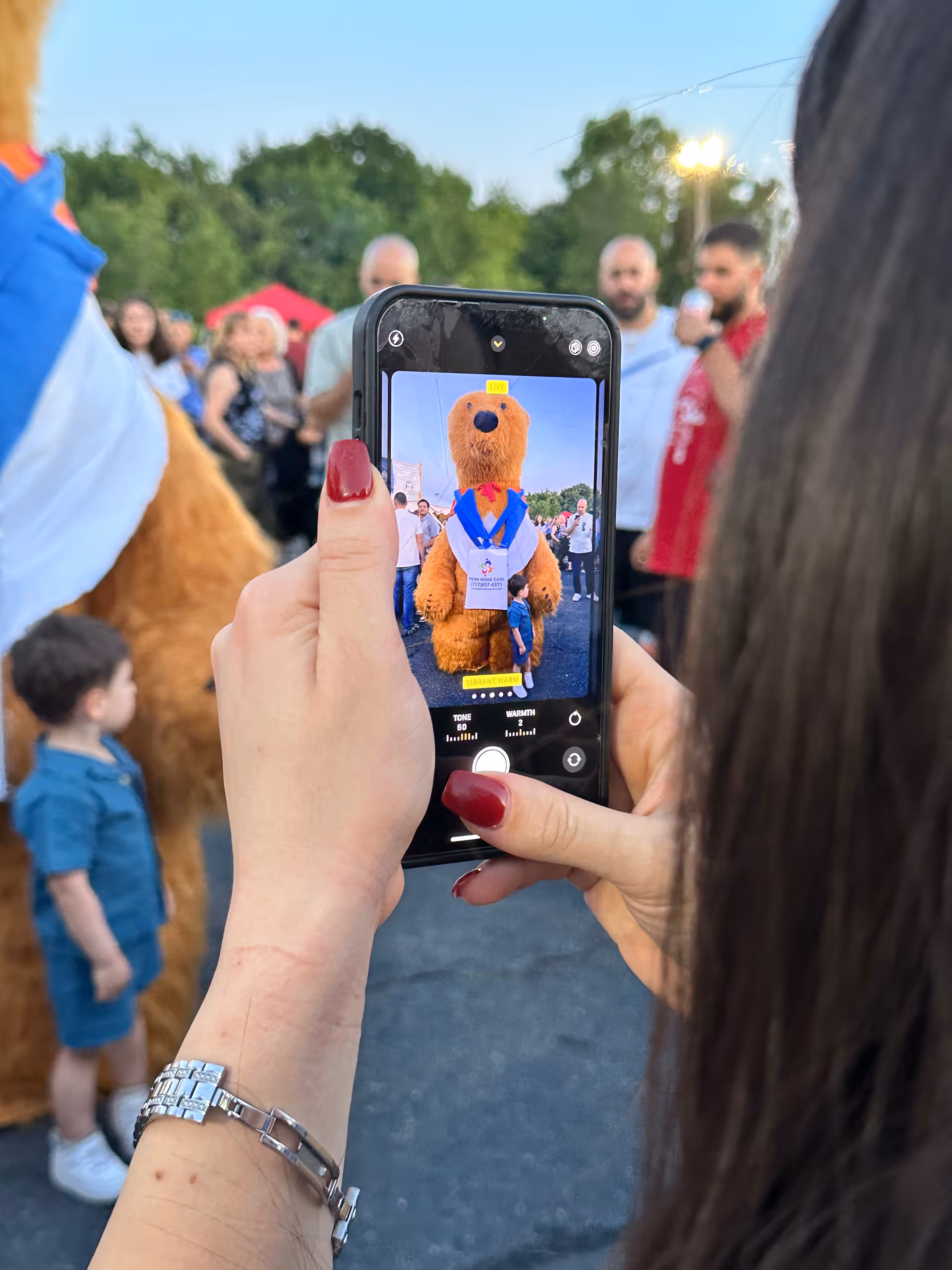 Person holds smartphone taking a photo of a bear mascot at an outdoor event