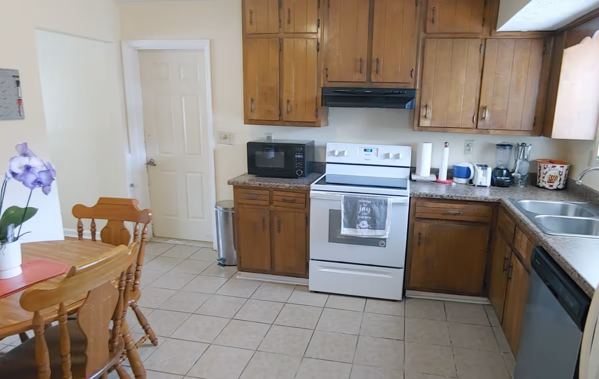 Kitchen with wooden cabinets, stove, sink, microwave, and dining table.