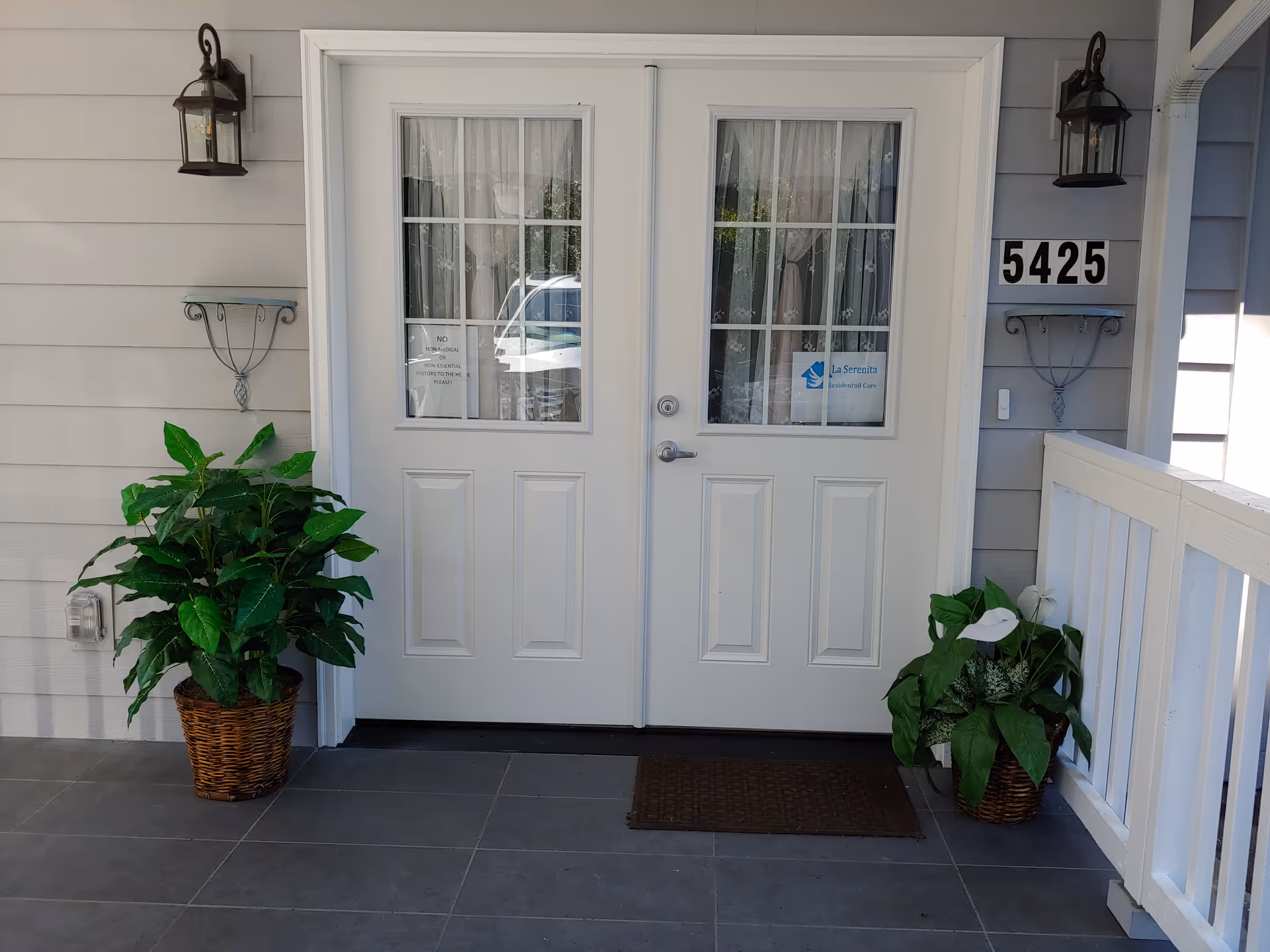 White double doors with glass panes, lanterns, and potted plants at the entrance.