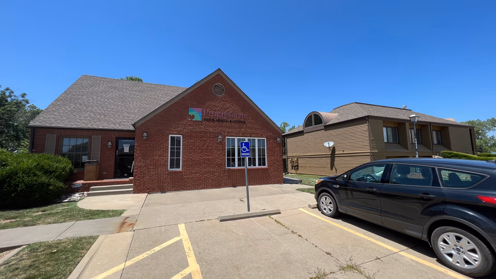 Brick building labeled Progressive Home Health & Hospice with handicap parking sign and a parked car.