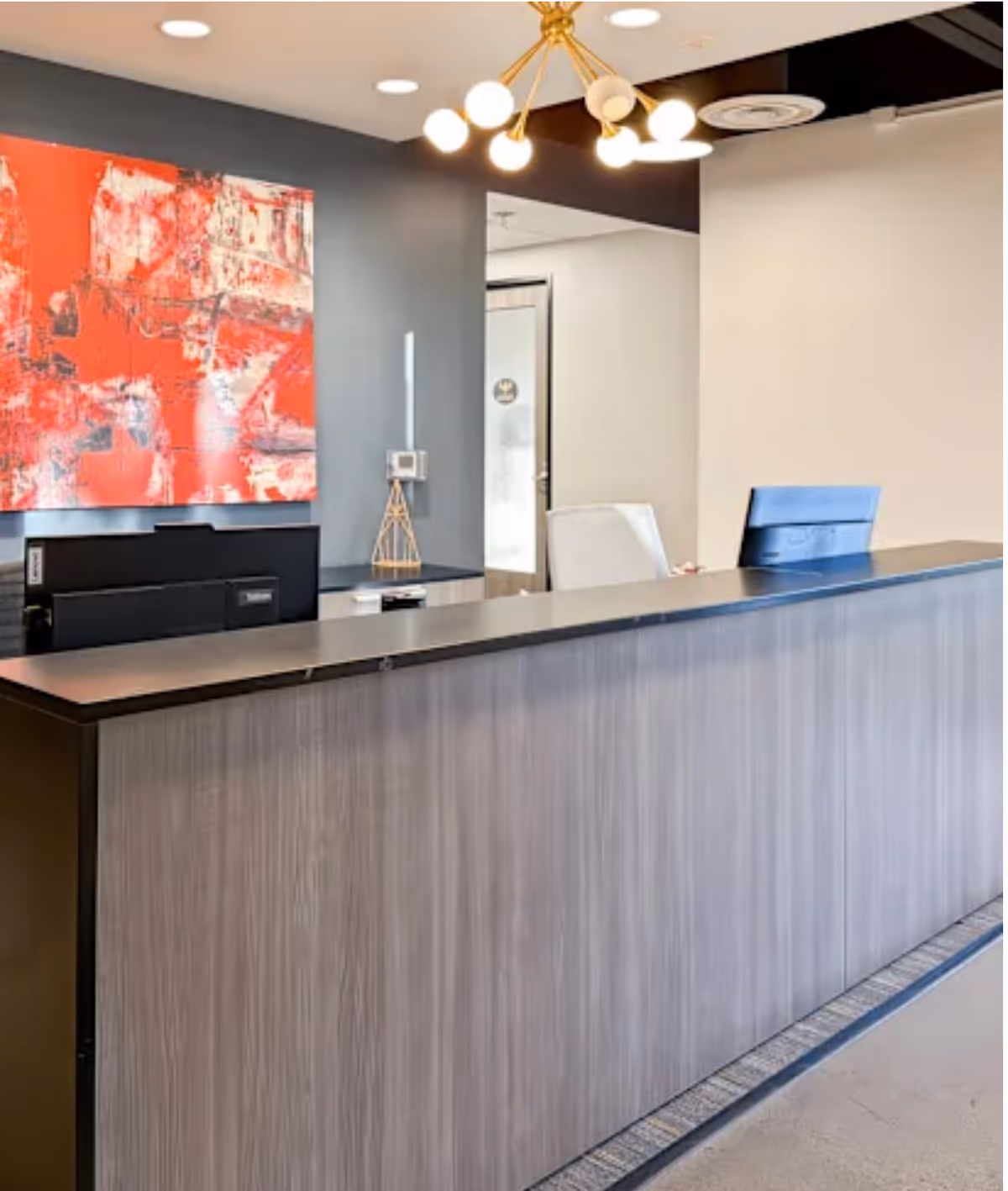 Bright reception desk area with abstract painting, modern chandelier, and doorway in lobby.