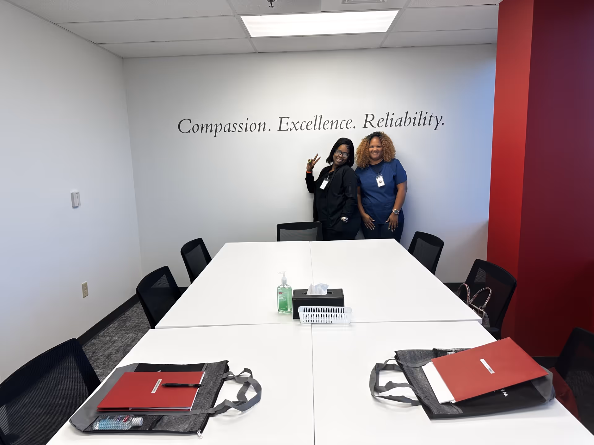 Two staff members pose in a conference room beneath a wall slogan.