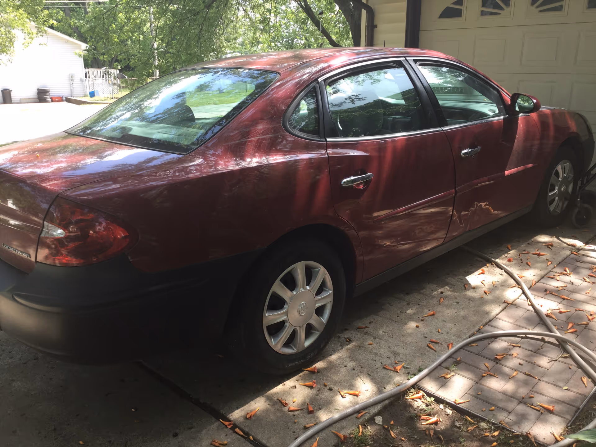 A red sedan parked in a driveway beside a garage under trees.