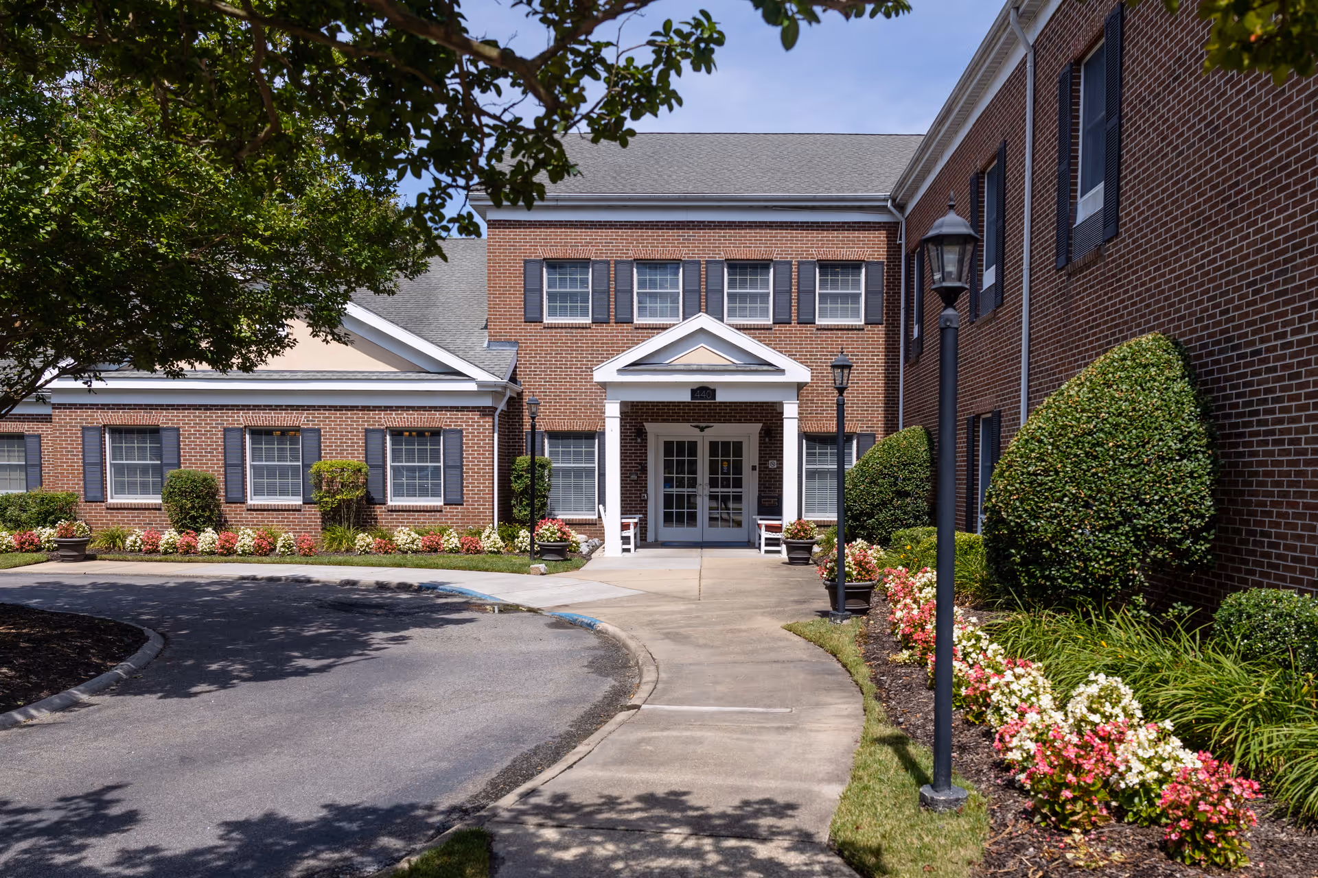 Brick senior living facility front entrance with landscaped shrubs and walkway.