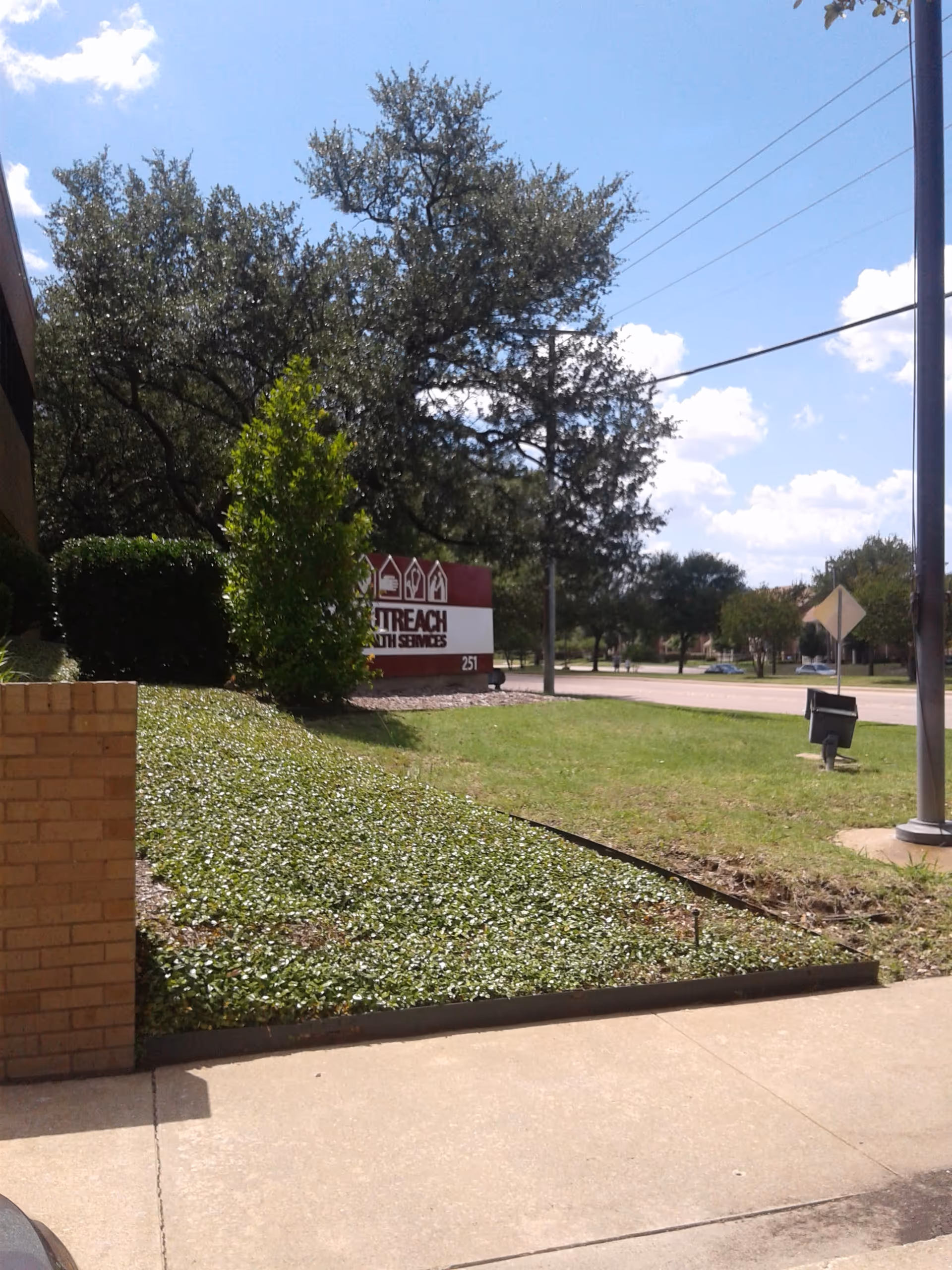 Outdoor view of Outreach Health Services sign with trees and landscaping.