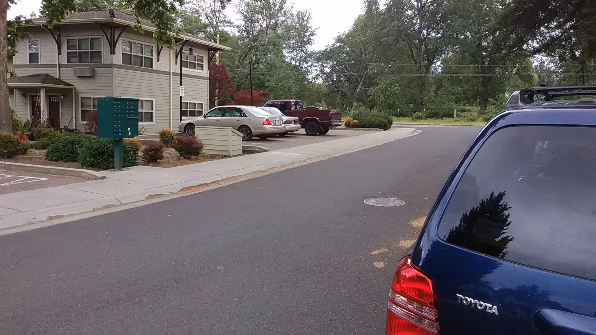 Two story senior living building with driveway, parked cars, and surrounding greenery.