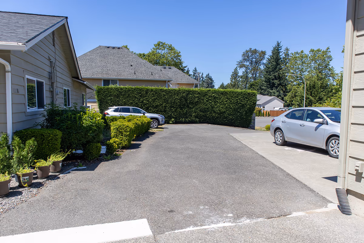 Exterior view of a senior living facility with parked cars and trimmed hedges.