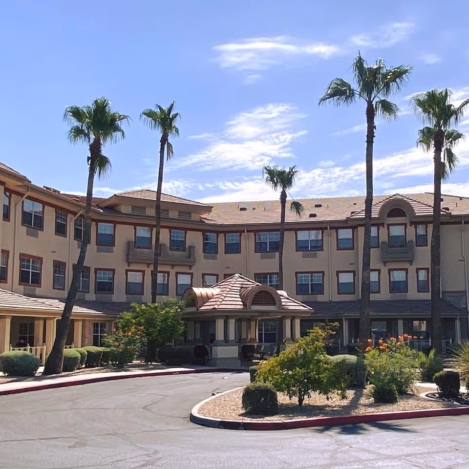 Exterior view of a beige senior living building with palm trees and a circular driveway.