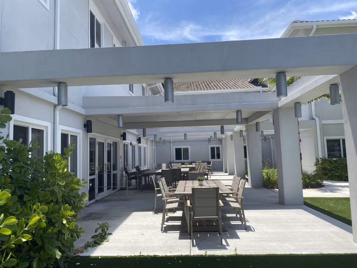 Outdoor patio area with tables and chairs under a covered walkway beside the building.