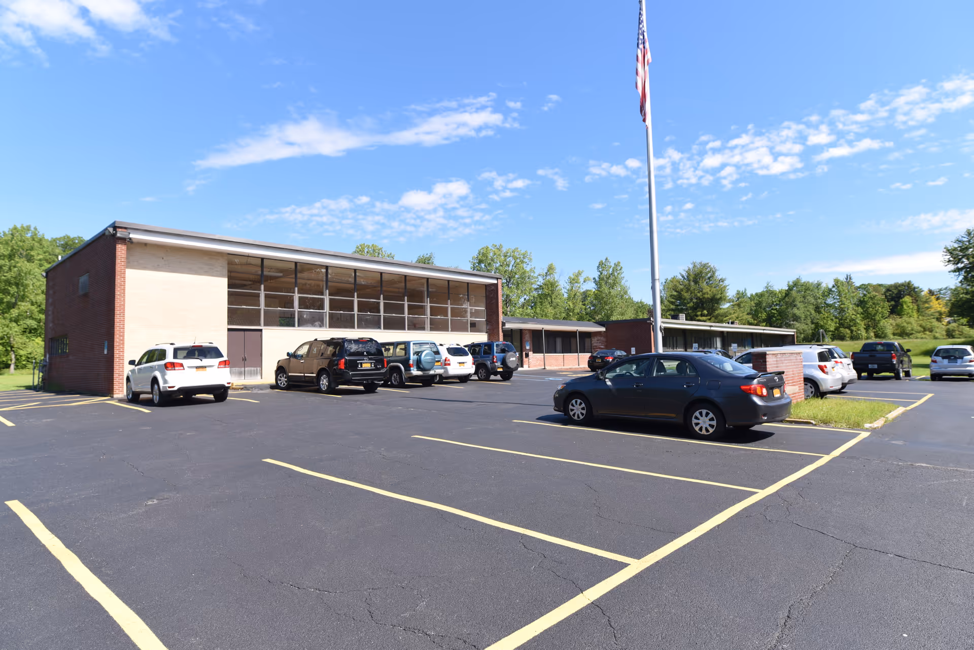 Exterior of a single-story brick senior care facility with large windows, flagpole, and parking lot.