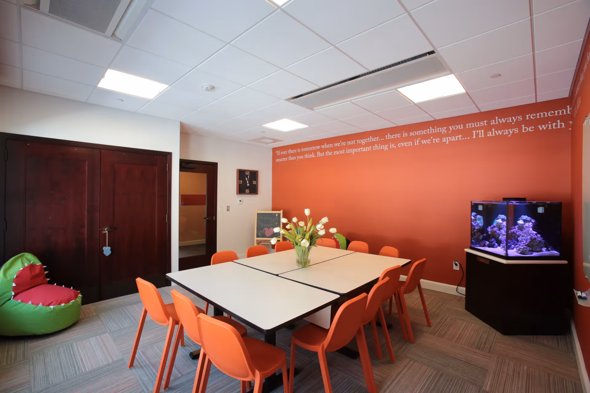 Bright multipurpose room with orange chairs around a rectangular table and a fish tank.