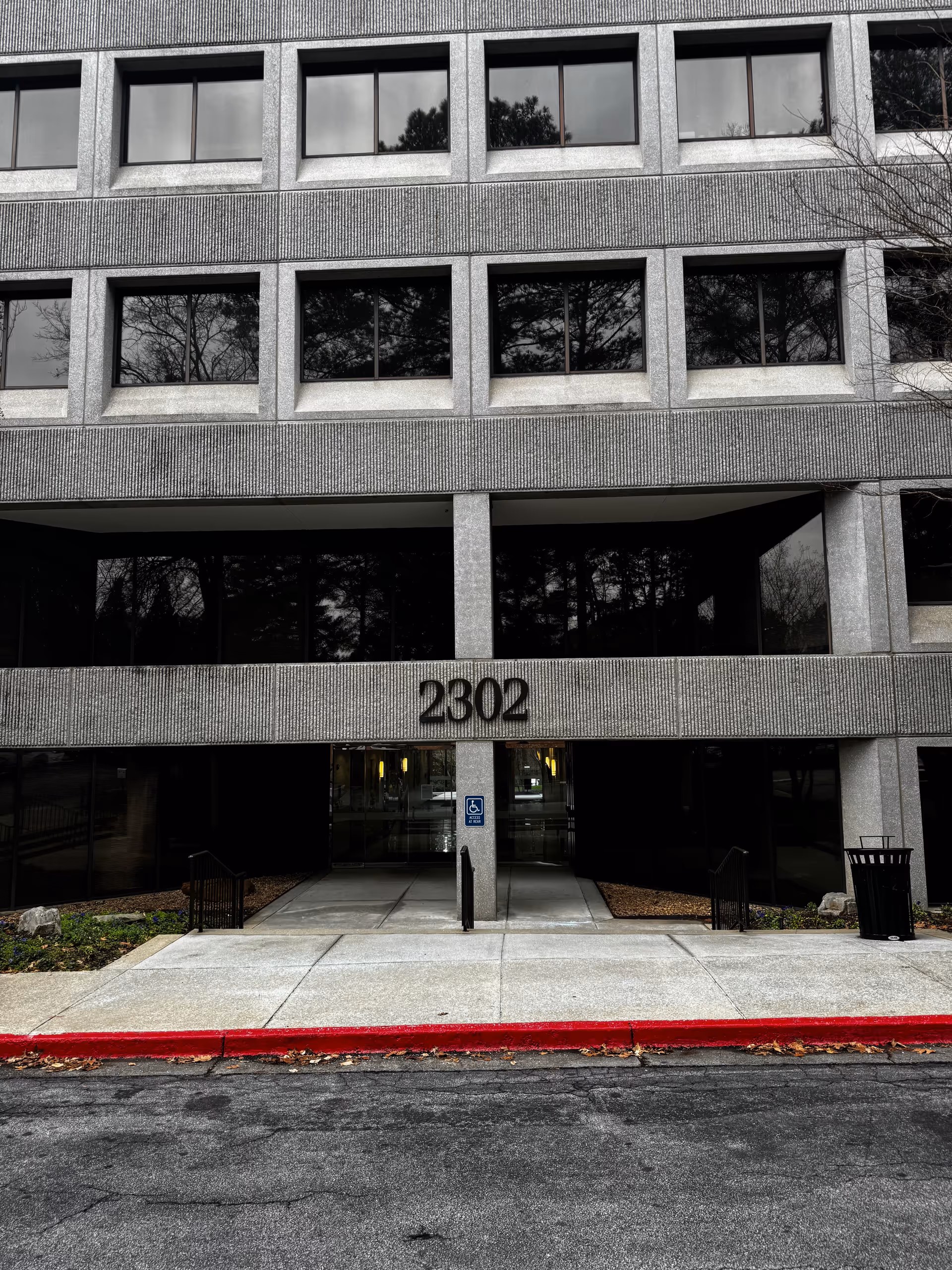 Grey concrete building front with large windows, entrance marked 2302, handicap sign.