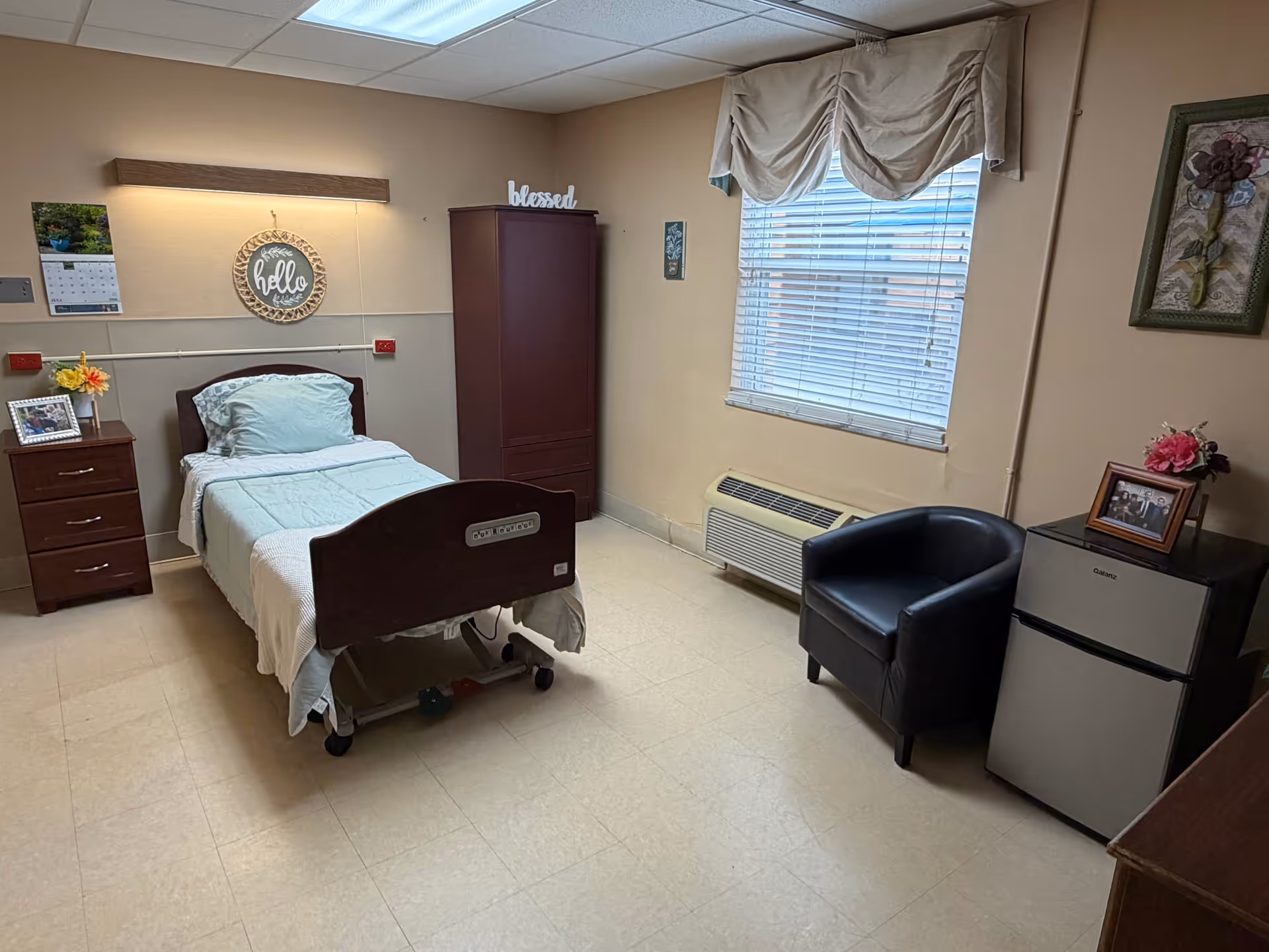 Senior living bedroom with a hospital-style bed, dresser, wardrobe, and window.