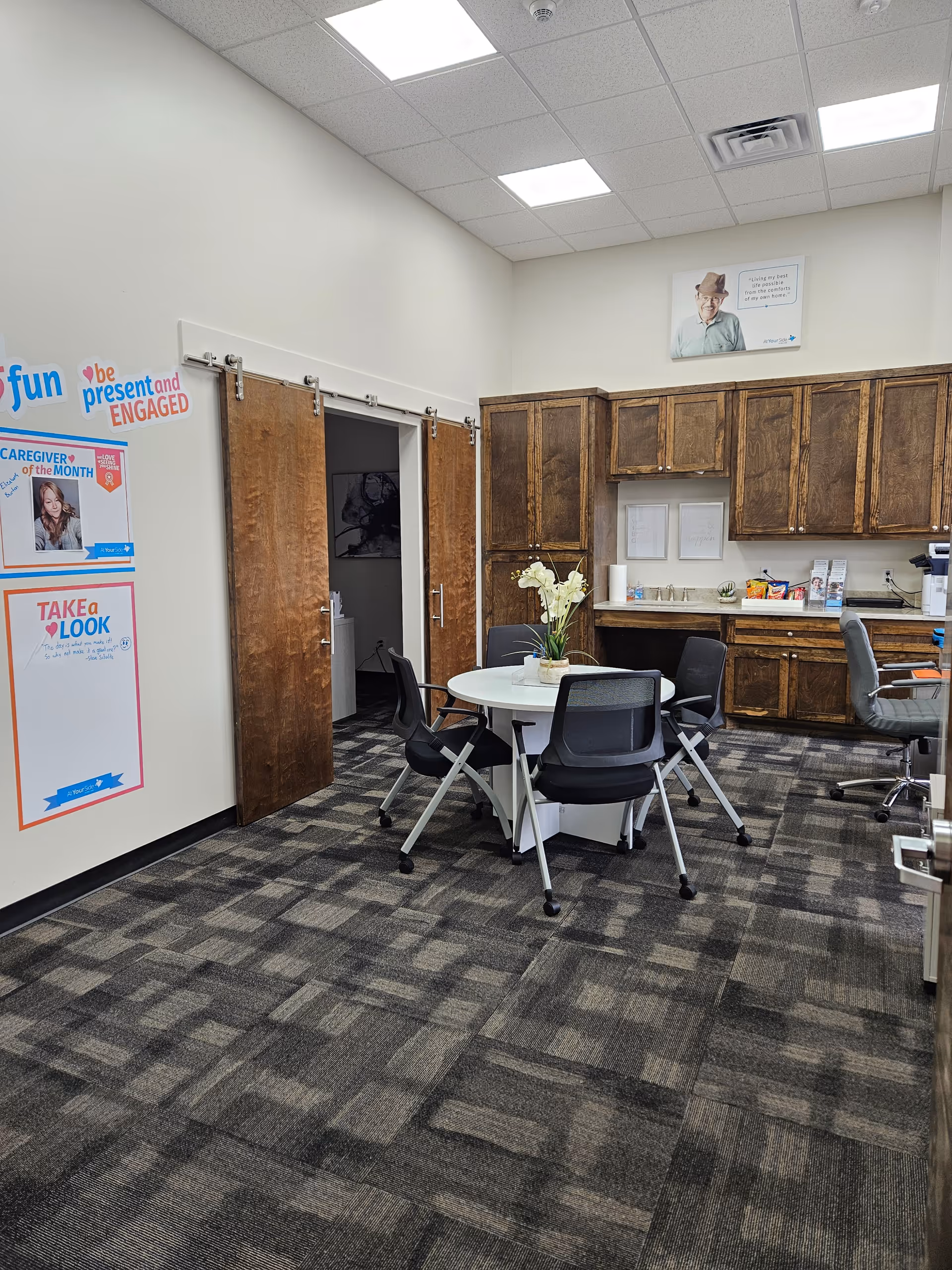 Common area with round table, chairs, wood cabinets, and posters on the walls.
