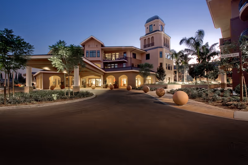 Exterior view of Walnut Village Orange County retirement community with entrance, tower, and illuminated pathway.
