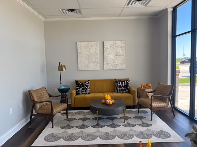 Cozy lounge with mustard sofa, two chairs, round coffee table, and abstract wall art.