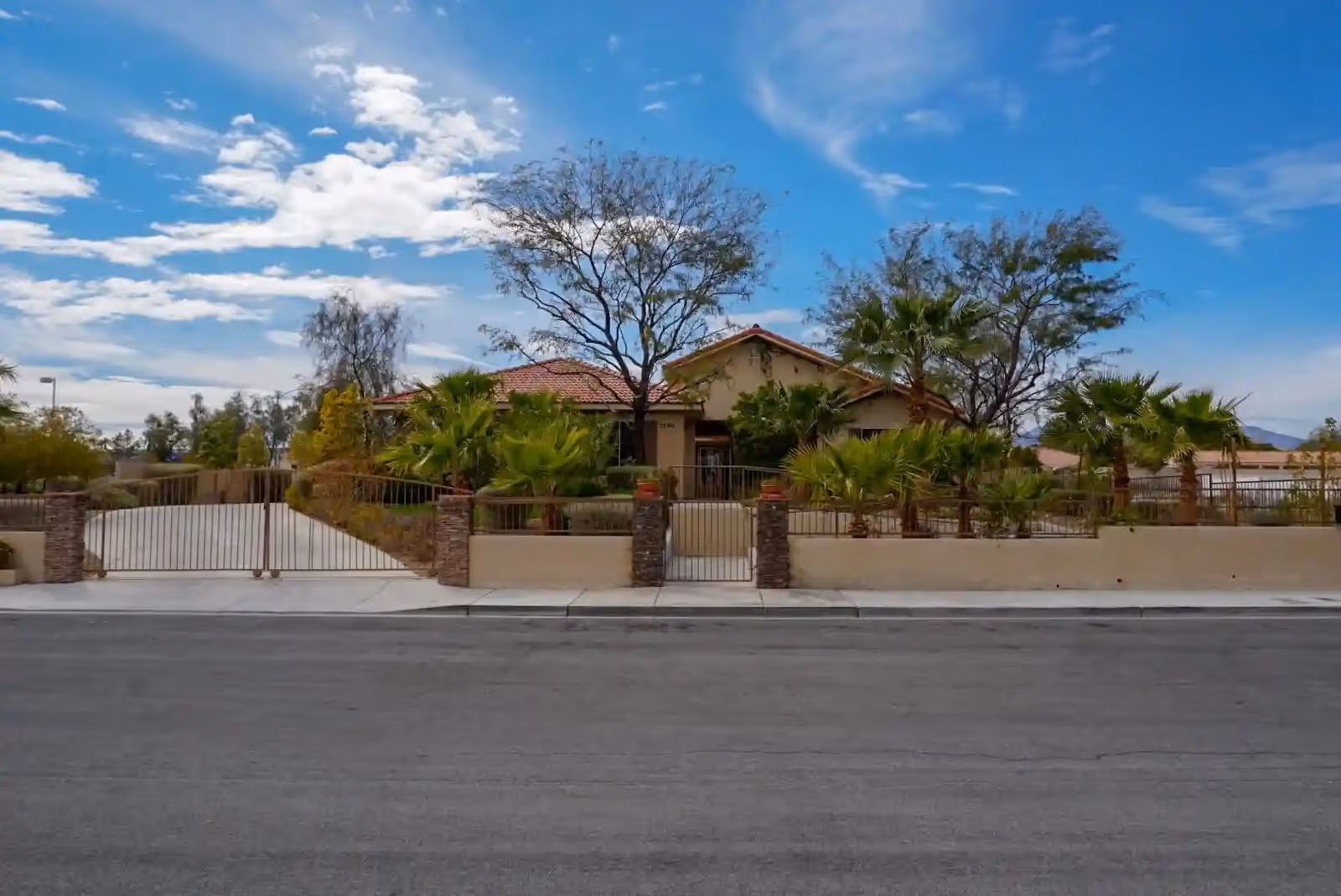 Front view of Nevada Memory Care facility with gate, palm trees, and desert landscaping.