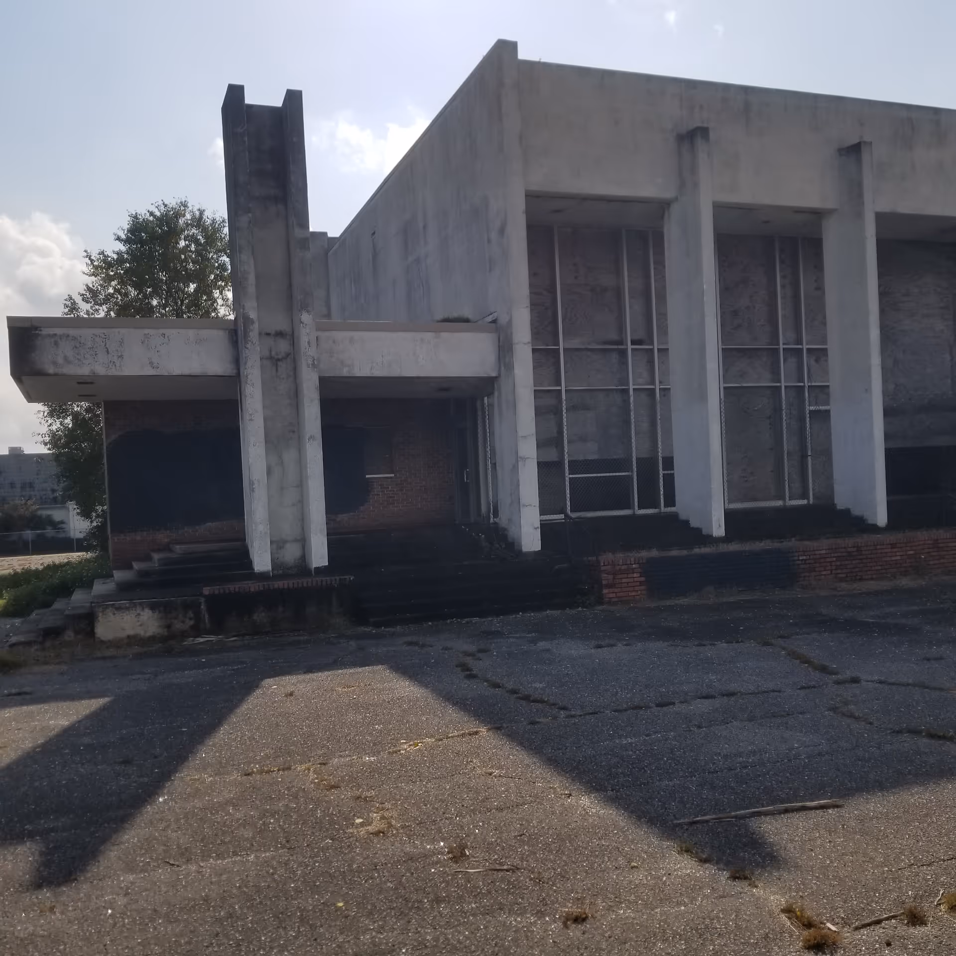 Abandoned concrete facility exterior with tall pillars and crumbling entry stairs.