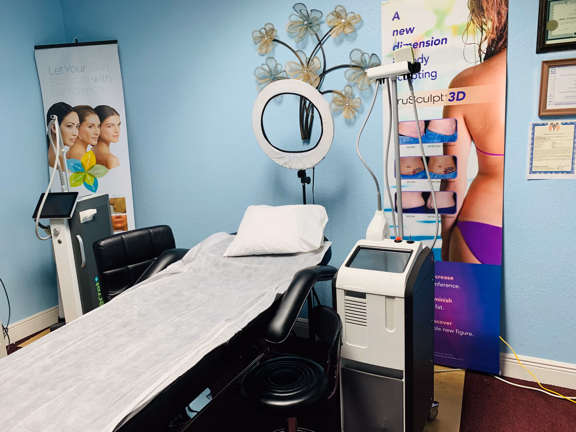 Examination room with a medical bed, ring light, and cosmetic treatment equipment.