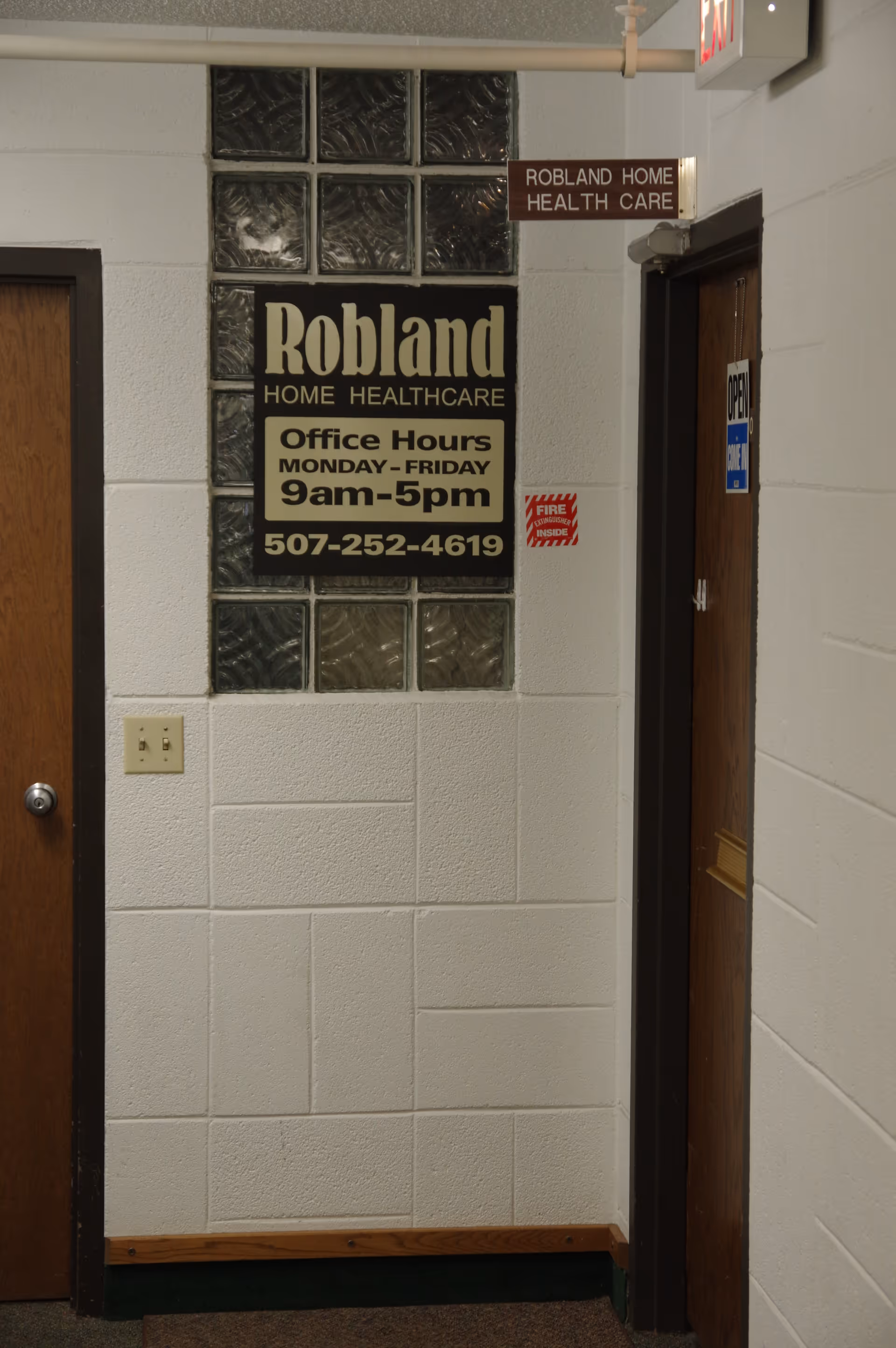 Indoor hallway with Robland Home Health Care sign, doorway, and bench along white tiled walls.