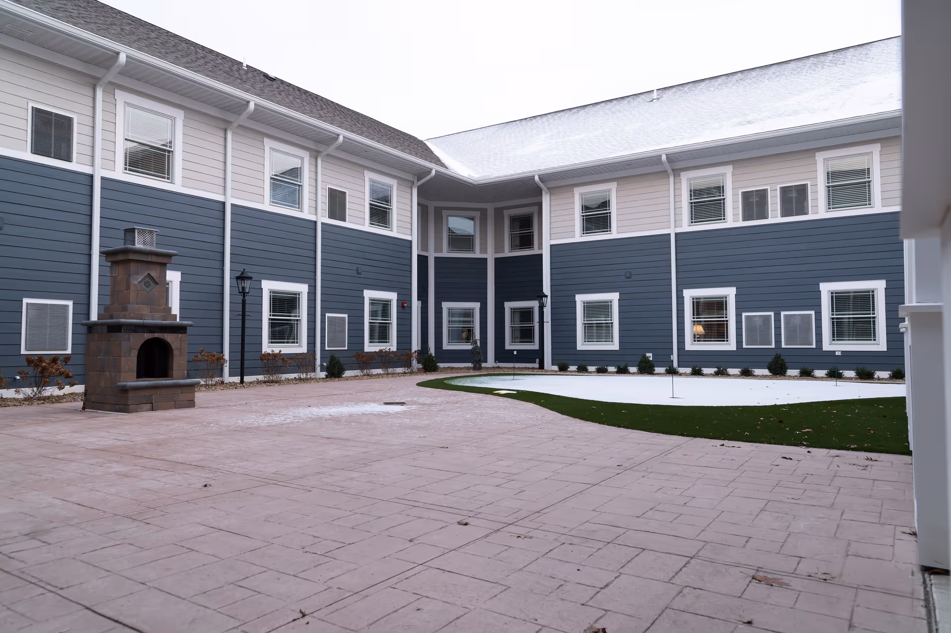 A U-shaped senior living facility courtyard with blue-gray siding and a brick outdoor fireplace.