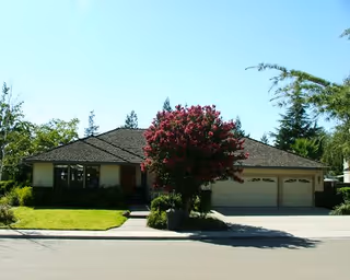 Single-story senior living facility with a front yard, flowering tree, and attached garage.