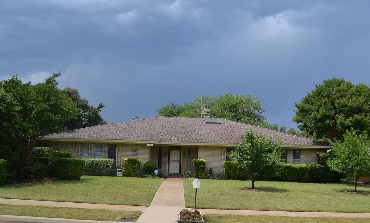 Single-story beige brick care home with front walkway, lawn, and trimmed shrubs.
