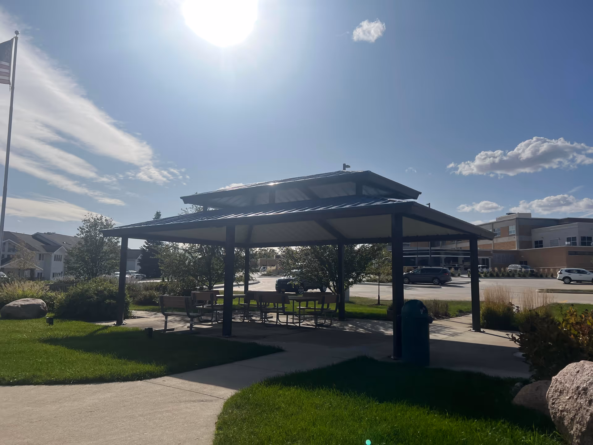 Outdoor pavilion with benches and tables in a sunny courtyard of a senior living facility.