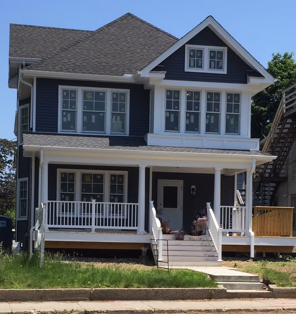 Blue two-story house with a white porch and front steps on a sunny day.